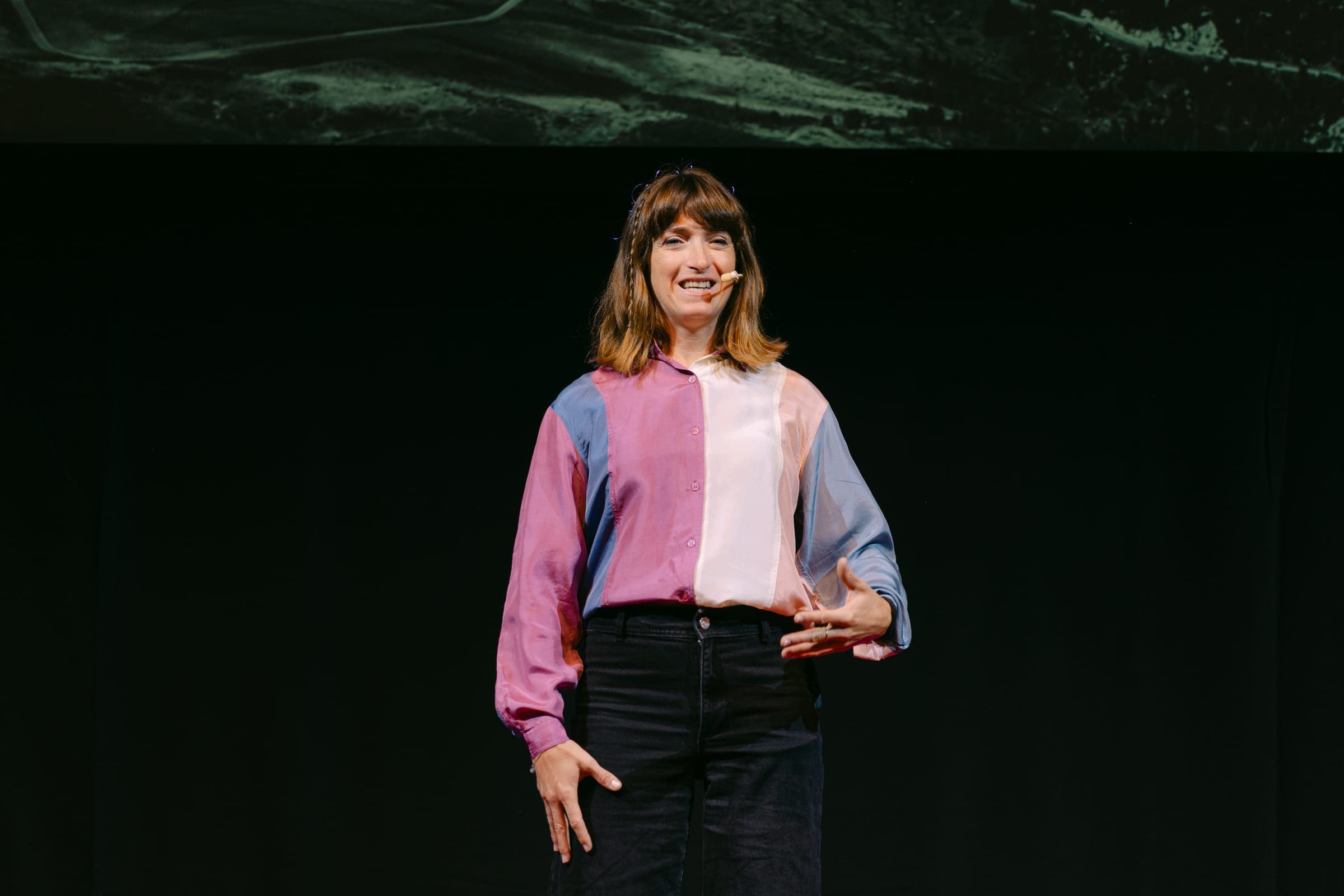 Martina Caironi parla sul palco di TEDxCortina 2025 con un microfono ad archetto e una camicia a blocchi di colore